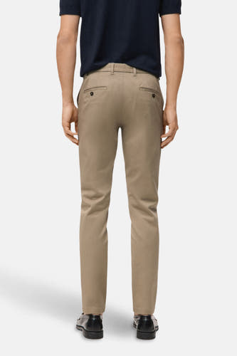 Beige chino van MANGO, gezien van achteren, gecombineerd met een donkerblauw poloshirt en zwarte schoenen.