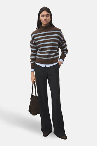 Sweat-shirt multicolore à col rond de MANGO, avec des rayures brunes et bleu clair, associé à une chemise bleue et un pantalon foncé.