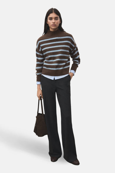 Sweat-shirt multicolore à col rond de MANGO, avec des rayures brunes et bleu clair, associé à une chemise bleue et un pantalon foncé.
