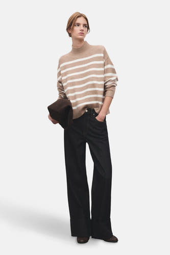 Pull beige à col rond de MANGO, rayé, associé à des jeans foncés avec des jambes larges et des chaussures marron.