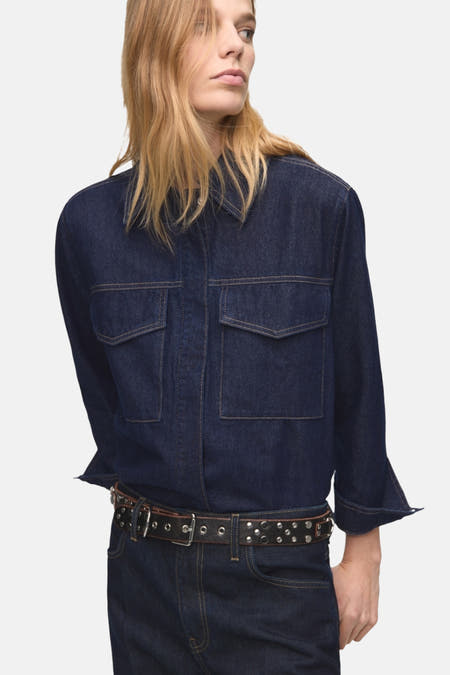Chemise en denim bleu marine à manches longues de MANGO, vue de derrière, avec un pantalon en denim bleu marine correspondant et des bottes brunes.