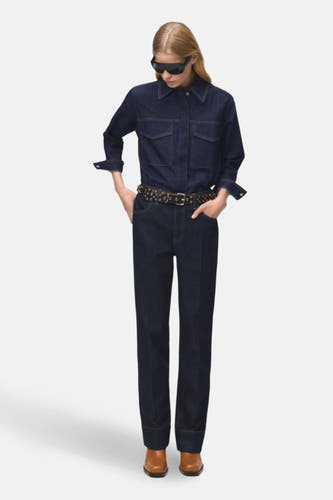 Chemise en denim bleu marine à manches longues de MANGO, avec deux poches po poitrine et portée avec une ceinture.