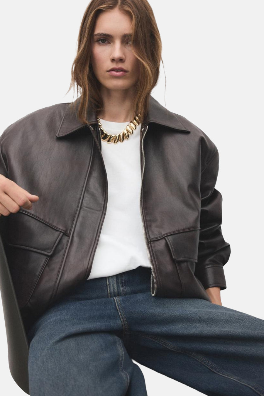 Collier court en or de MANGO, porté avec un t-shirt blanc et une veste en cuir marron.