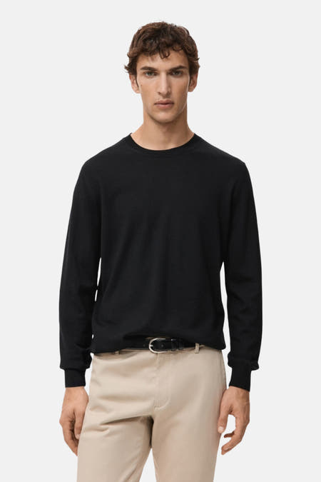 Pull noir avec col rond de MANGO, vu de derrière, associé à un pantalon beige.