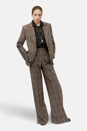 Blazer marron de MANGO, avec un motif à carreaux et porté avec une chemise sombre et des chaînes d'or.