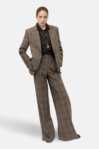 Blazer marron de MANGO, avec un motif à carreaux et porté avec une chemise sombre et des chaînes d'or.