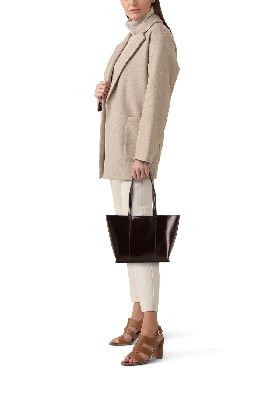 Sac à main marron de MANGO, porté par une femme avec un manteau beige et un pantalon blanc cassé avec des talons marron.