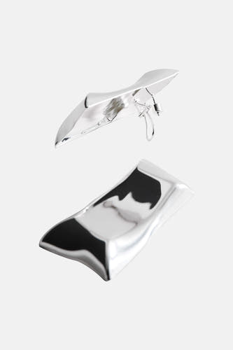 Boucles d'oreilles argentées de MANGO avec un design minimaliste et fluide, représentées dans une composition artistique.