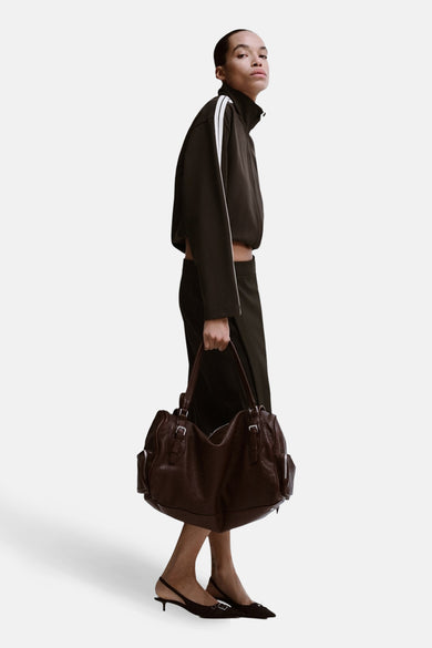 Gilet marron de MANGO porté avec un pantalon d'entraînement foncé et des rayures blanches et une poche marron.