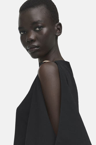 Chemisier noir sans manches de MANGO, avec une épaule dénudée et un décolleté doré.