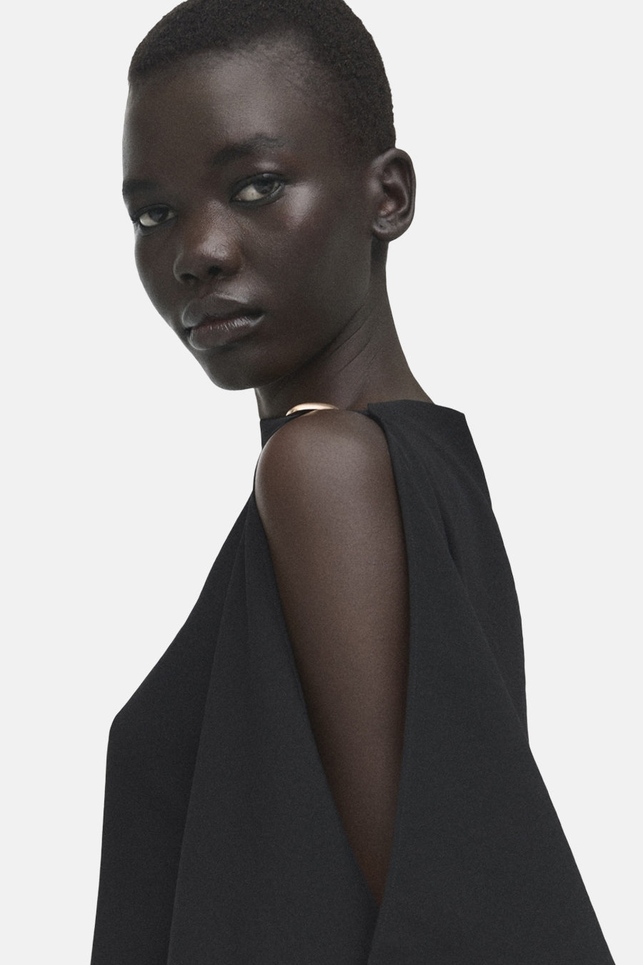 Chemisier noir sans manches de MANGO, avec une épaule dénudée et un décolleté doré.