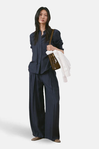 Chemise bleue à manches longues de MANGO, à motif craie, portée avec un pantalon assorti et un sac marron.