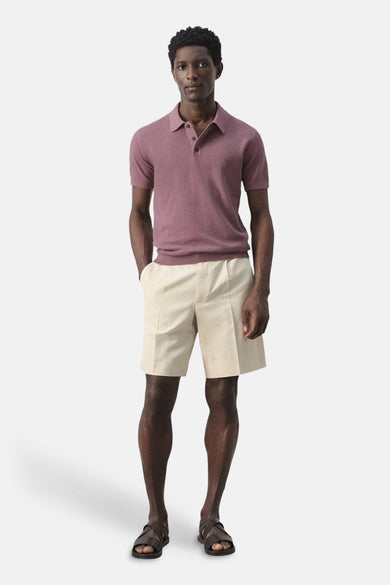 Polo violet MANGO, à manches courtes, porté avec un short beige et des sandales en cuir.