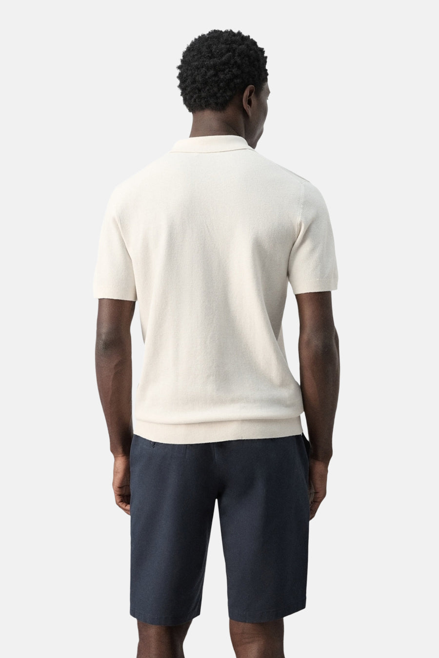 Ecru polo van MANGO, achterkant, met korte mouwen en donkerblauwe shorts.