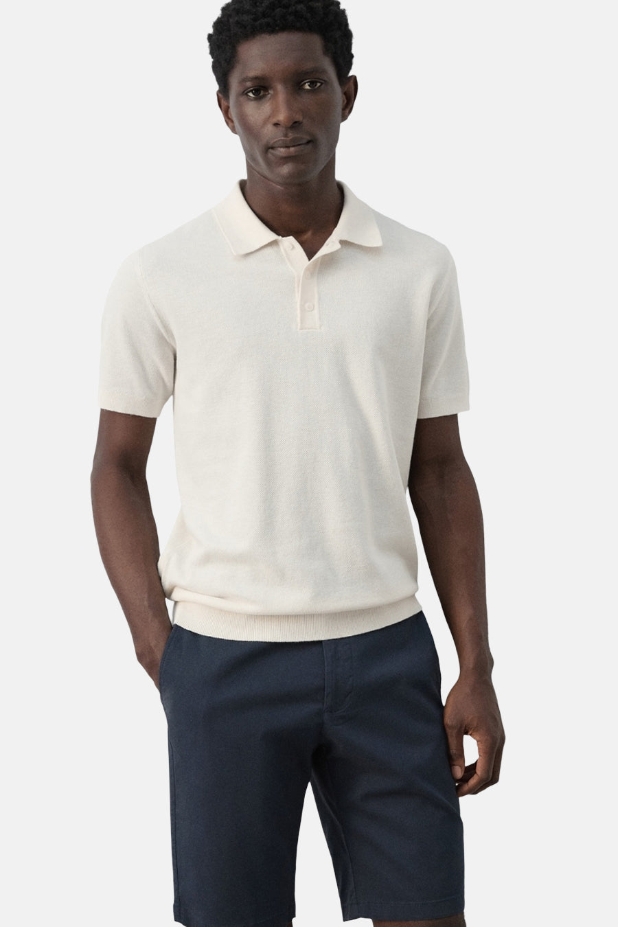 Polo écru de MANGO, à manches courtes et portée avec un short bleu marine.