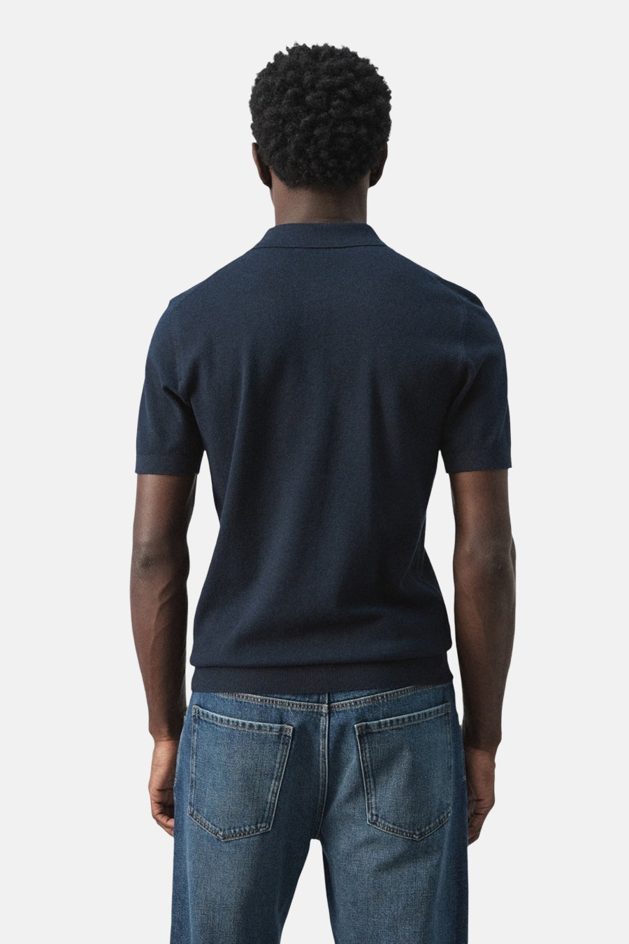 Blauwe polo van MANGO, achterkant gezien, gecombineerd met een jeansbroek.
