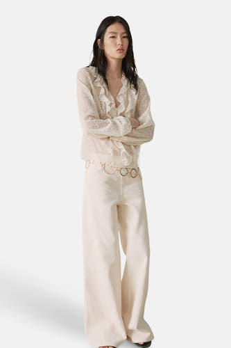 Chemisier écru à manches longues de MANGO avec volants et motif à pois subtil, combiné avec un pantalon large et une ceinture dorée.