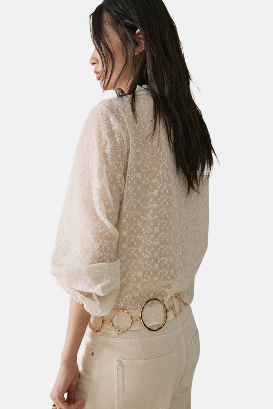 Ecru blouse met lange mouwen van MANGO met geborduurd bloemenpatroon en ruffle kraag, gecombineerd met jeans en een gouden ceintuur.