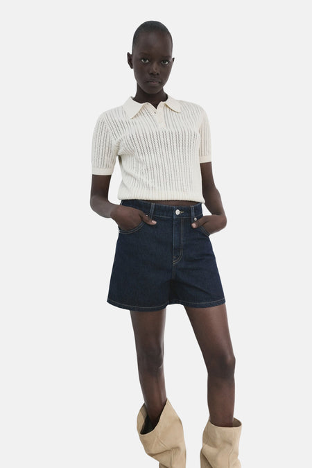 Bermuda short en jean bleu marine de MANGO, combinée avec un polo en crochet et des bottes beiges.