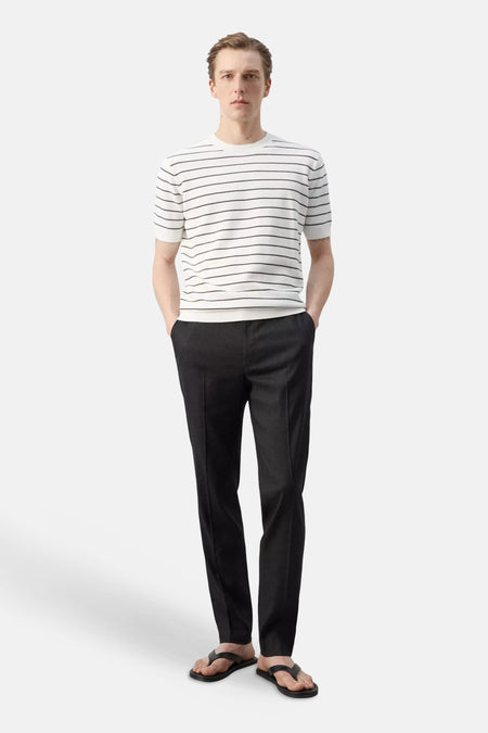 T-shirt à manches courtes, blanc à rayures noires de MANGO, porté par un mannequin avec un pantalon foncé et des tongs noires.