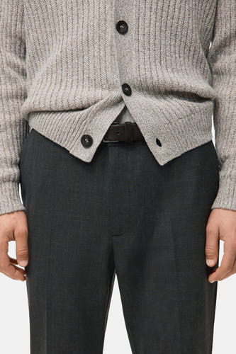 Pantalon gris de MANGO, avec un motif de carreaux subtil et une texture lisse, porté avec un gilet tricoté et une ceinture en cuir.