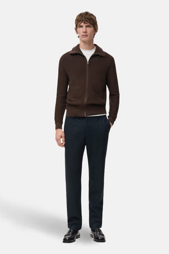 Pantalon bleu de MANGO, associé à une veste brune avec fermeture éclair et des chaussures noires.