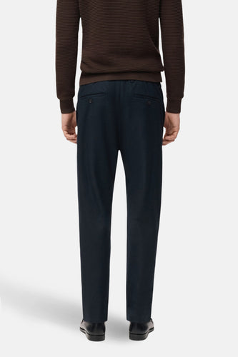 Man van achteren, bruine trui, blauwe broek.