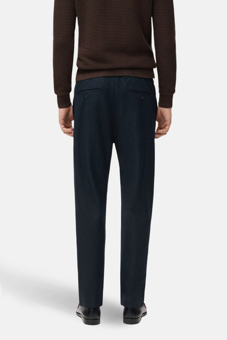 Man van achteren, bruine trui, blauwe broek.