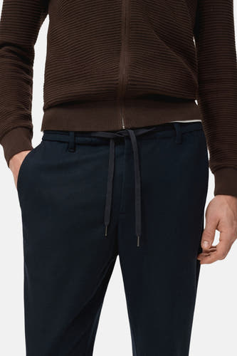 Pantalon bleu de MANGO, avec cordon de serrage et poche sur le côté, associé à une veste brune.