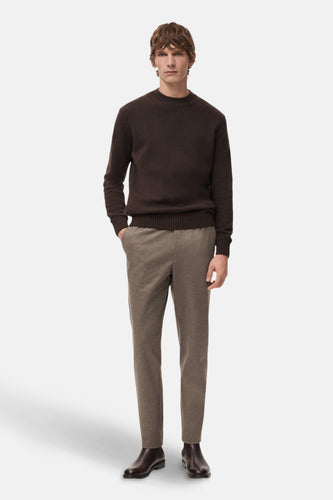 Man met bruine trui, beige broek en bruine schoenen, staand.