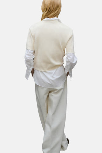 Ecrukleurige trui met ronde hals van MANGO, met daaronder een wit overhemd en een crèmekleurige broek.