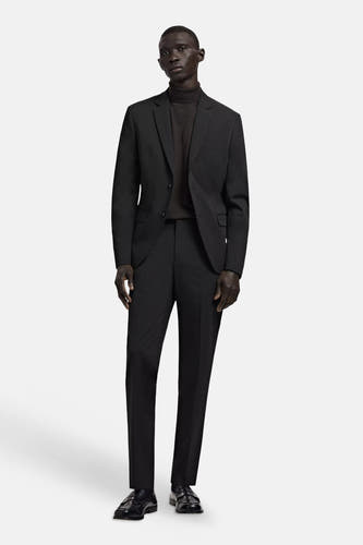 Blazer noire MANGO à deux boutons, portée sur un col roulé foncé avec un pantalon assorti et des mocassins.