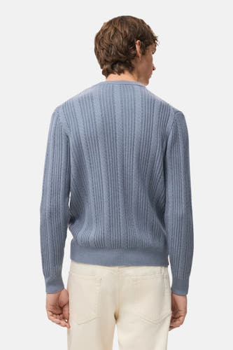 Blauwe trui met ronde hals van MANGO, met ribbeltextuur op de rug en crèmekleurige broek.
