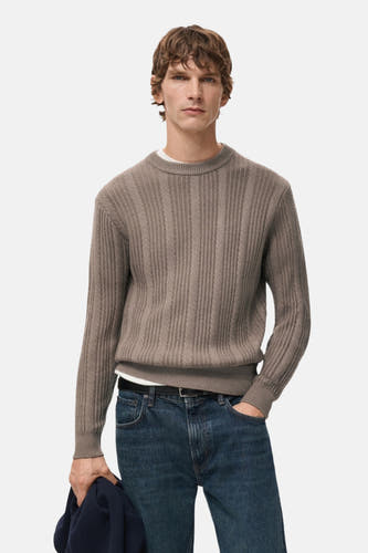 Pull marron avec col rond de MANGO, avec une structure côtelée sur le dos et un blouson bleu foncé en main.