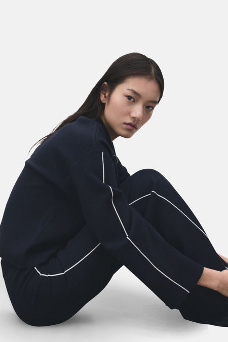 Vrouw in donkerblauw joggingpak met witte bies, zittend op de grond.