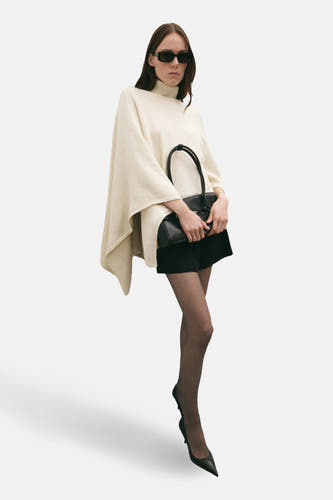 Poncho écru de MANGO, porté avec un sac noir, des sous-vêtements noirs et des escarpins noirs.