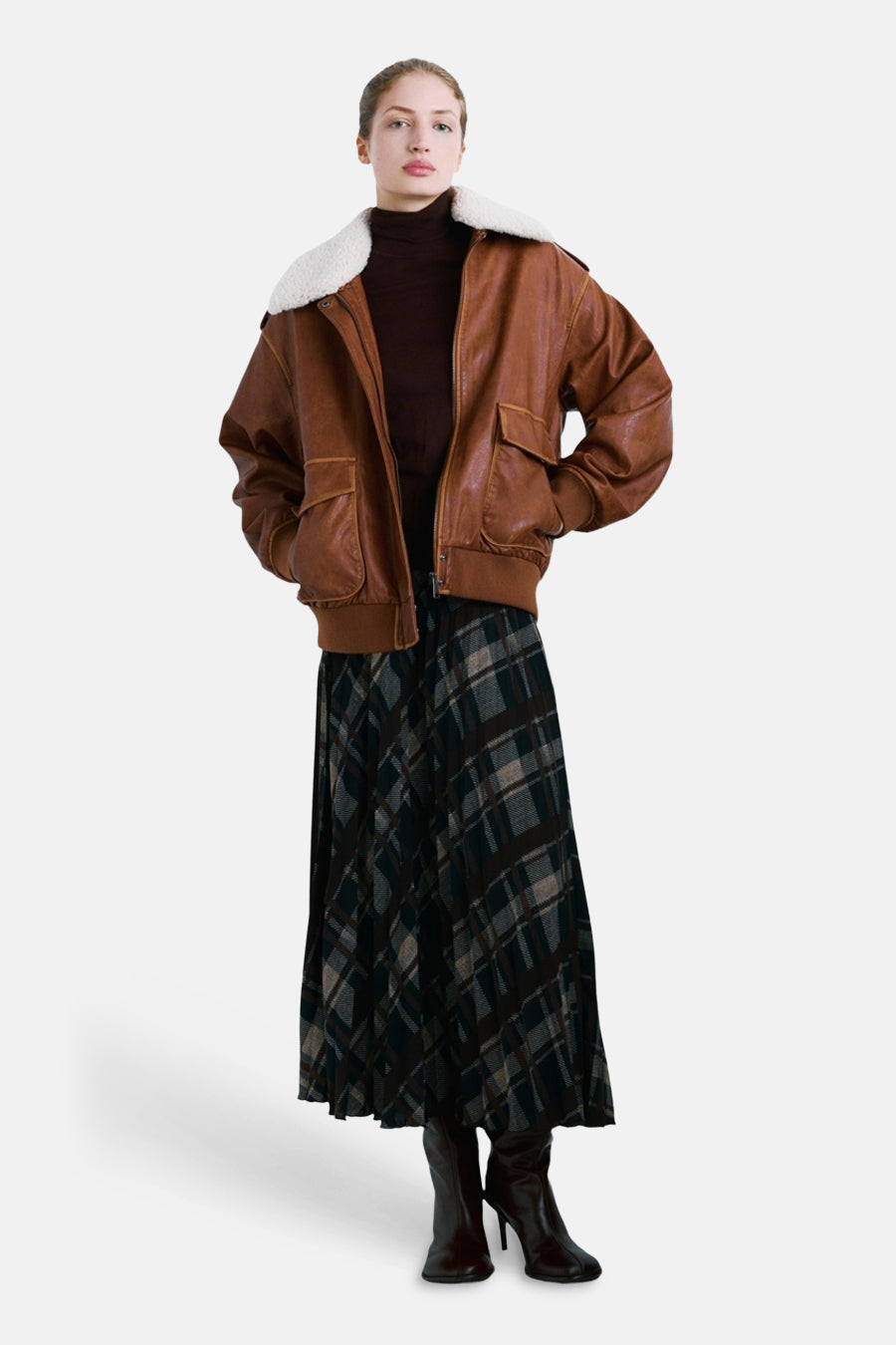 Manteau marron de MANGO, avec un col blanc et des poches, combiné avec une jupe à carreaux et des bottes.