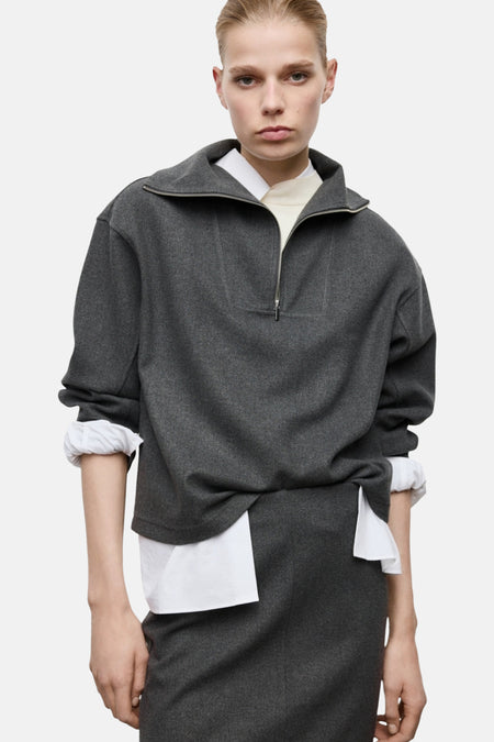 Grijze wollen trui met rits en witte blouse.
