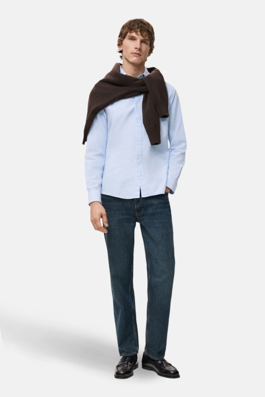 Man in blauw overhemd, donkere spijkerbroek en bruine trui.
