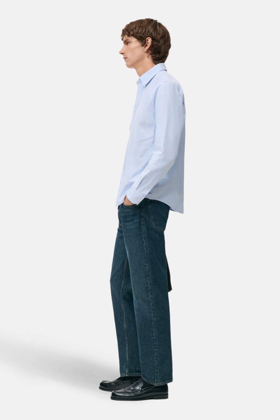 Man in blauw hemd en jeans, staand in profiel.