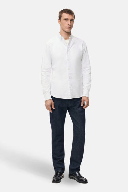 Een man in een wit overhemd, donkere jeans en zwarte schoenen staand.