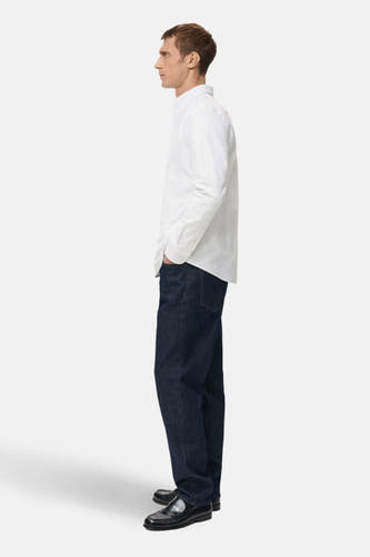 Blouse blanche à manches longues de MANGO, portée en vue latérale avec des jeans foncés et des loafers noirs.