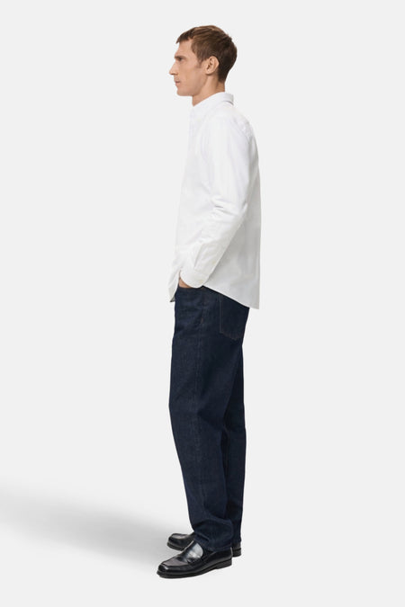 Man in witte blouse, donkere jeans en zwarte schoenen.