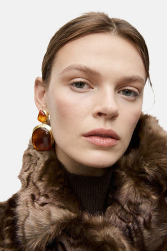 Boucles d'oreilles en or de MANGO, avec des accents ambre et un collier brun.