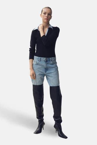 Pull-over V-hals bleu de MANGO, porté avec des jeans bleus et des bottes noires en cuir jusqu'aux genoux.