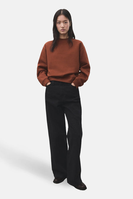 Vrouw met bruine trui en zwarte jeans.