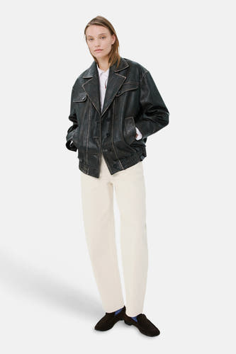 Jean en denim blanc coupe spéciale de MANGO, combiné avec une veste en cuir noir et des mocassins foncés avec des chaussettes bleues.