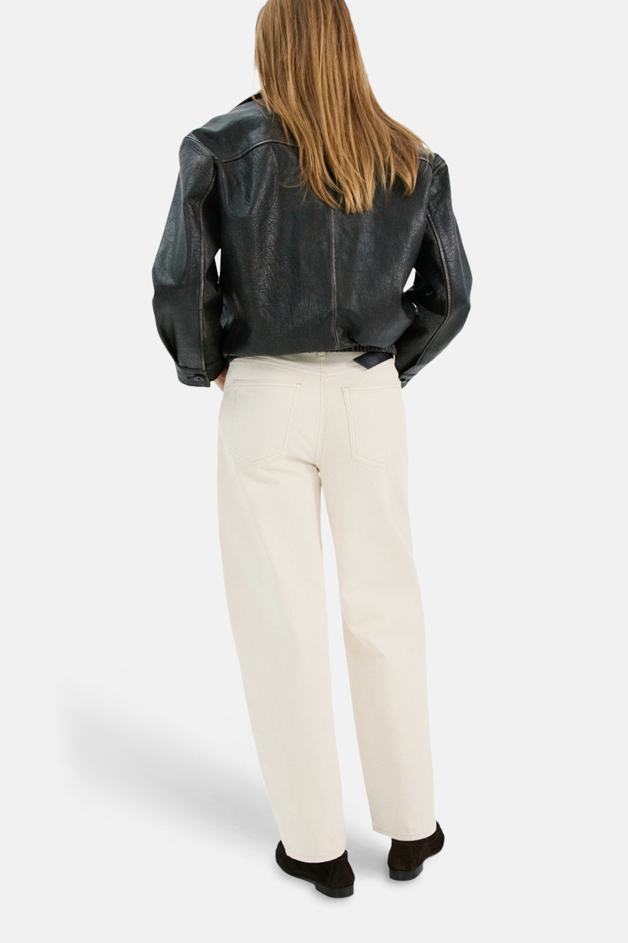 Witte denim jeans special fit van MANGO, gezien van achteren, met zwarte leren jas en suède schoenen.

