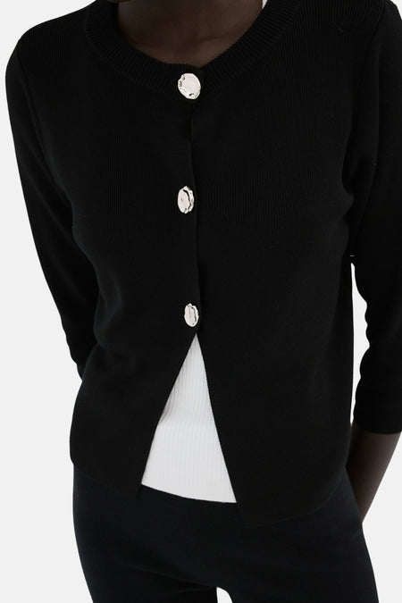 Gilet noir de MANGO, vu de dos, avec des manches trois-quarts et un haut blanc en dessous.