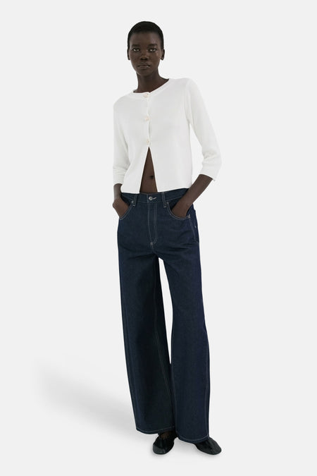 Gilet blanc de MANGO, porté ouvert sur un ventre visible et un jean bleu foncé à jambes larges.